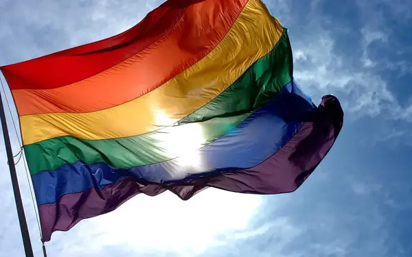 LGBTQ Flag flying in blue skies with bright sun shining through