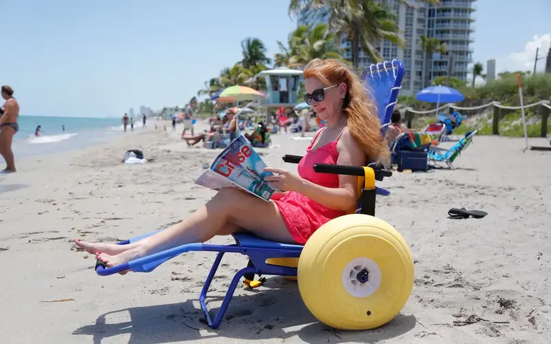 Woman in beach wheelchair reading a magazine by the water